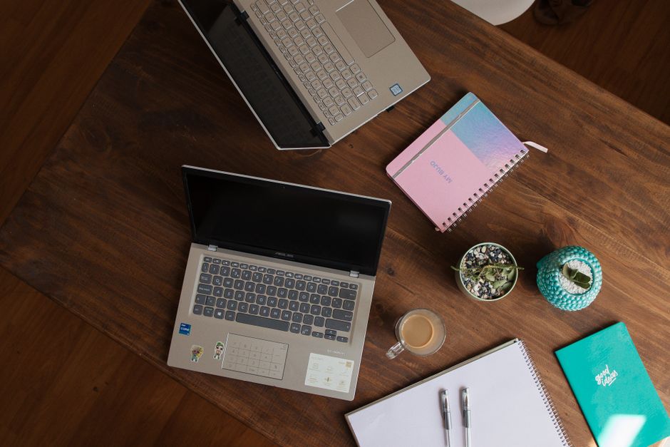 Top view of a wooden desk with laptops, notebooks, coffee cup, and potted plant. Ideal for office or study themes.