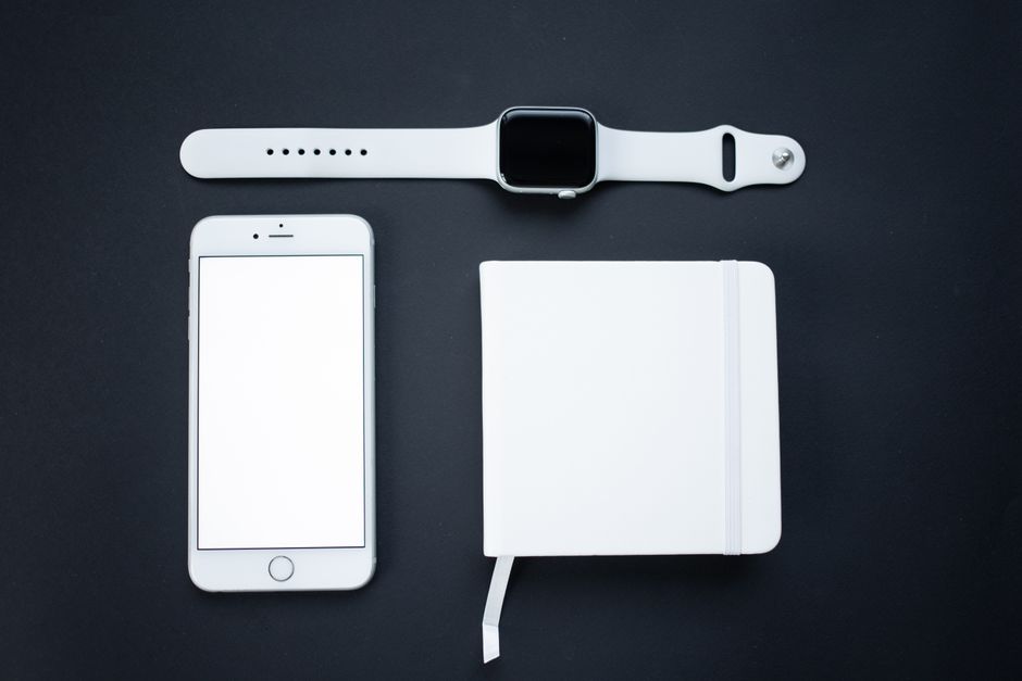 Minimalist top view of a smartphone, smartwatch, and notepad on a dark background, perfect for tech and lifestyle themes.